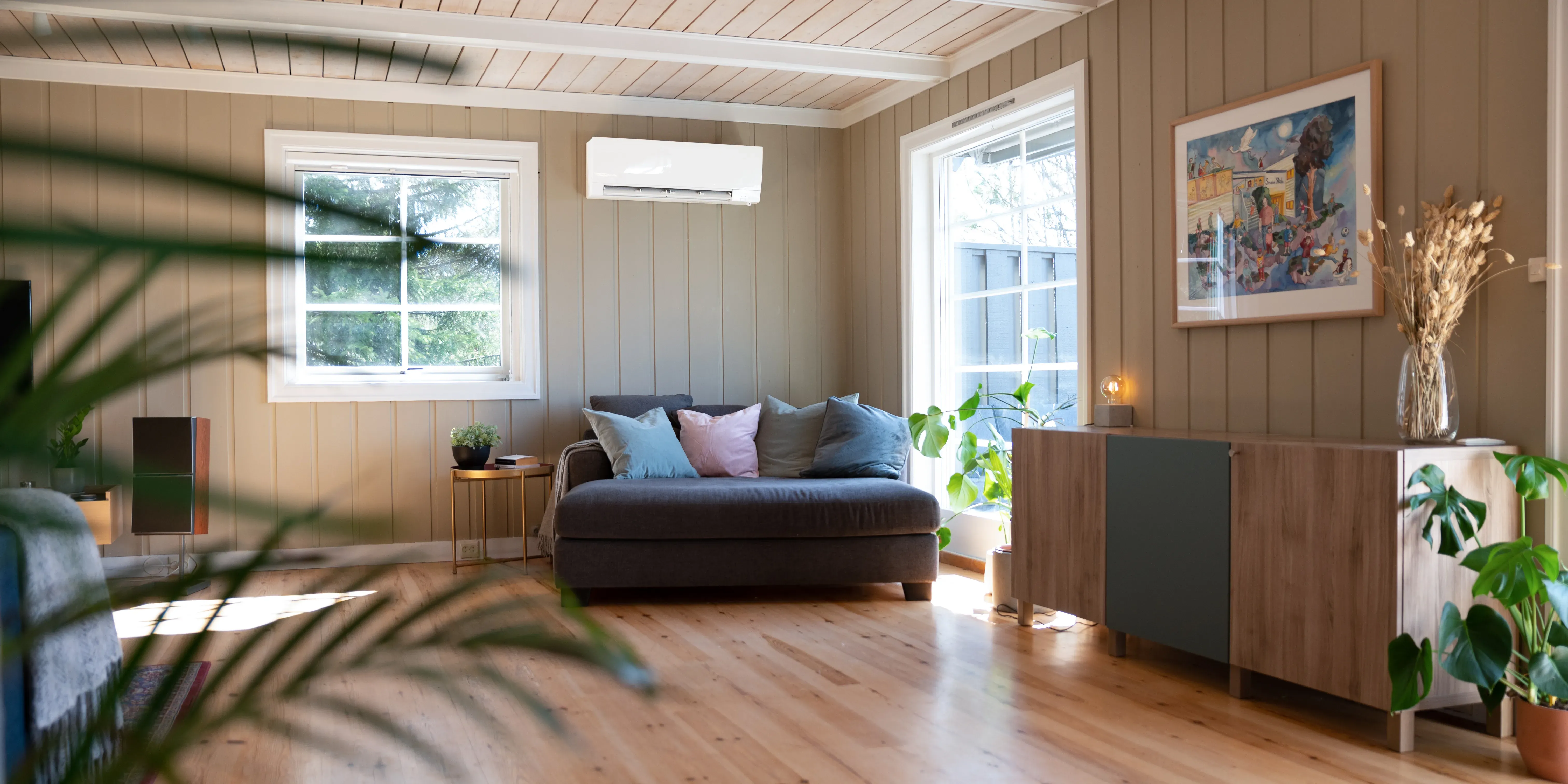 Veggmontert varmepumpe i moderne stue med sofa og planter.