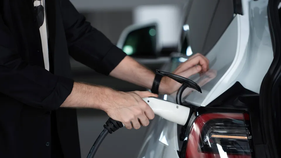 Bilde av en hånd med elbillader som plugges inn i bilen
