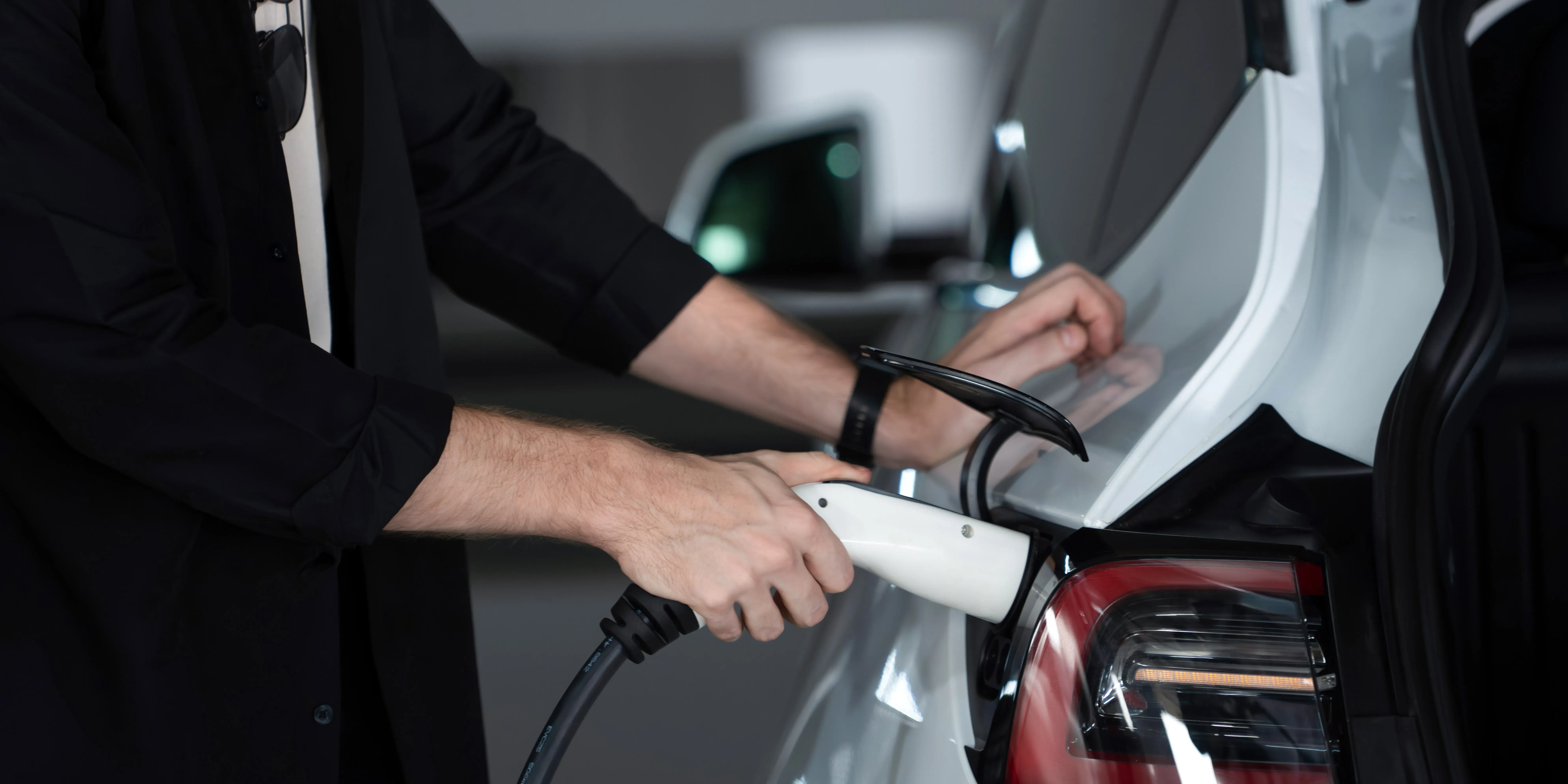 Bilde av en hånd med elbillader som plugges inn i bilen