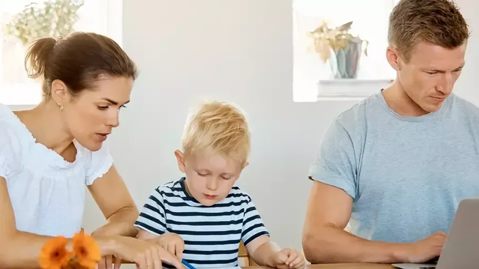 Familj med litet barn använder bärbar dator tillsammans vid bord.