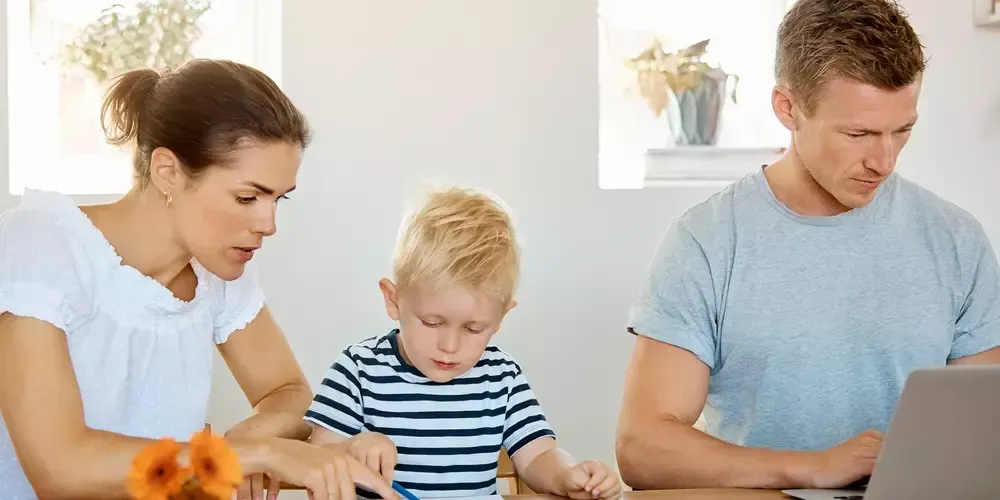 Familj med litet barn använder bärbar dator tillsammans vid bord.