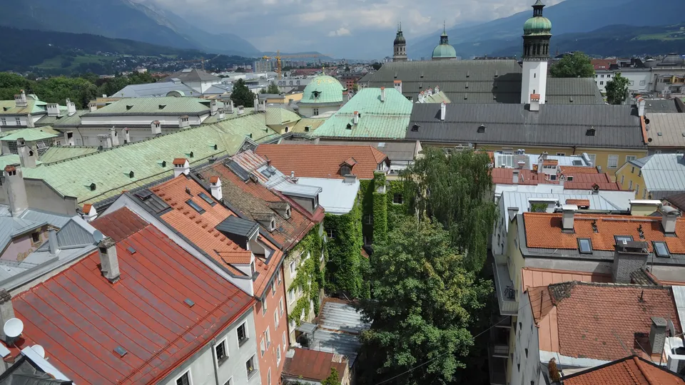 Blick über die Dächer der Innsbrucker Altstadt mit historischen Gebäuden, Kirchtürmen und den Tiroler Alpen im Hintergrund.