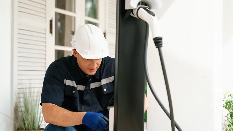 Técnico instalando um carregador de veículo elétrico na fachada de uma casa.