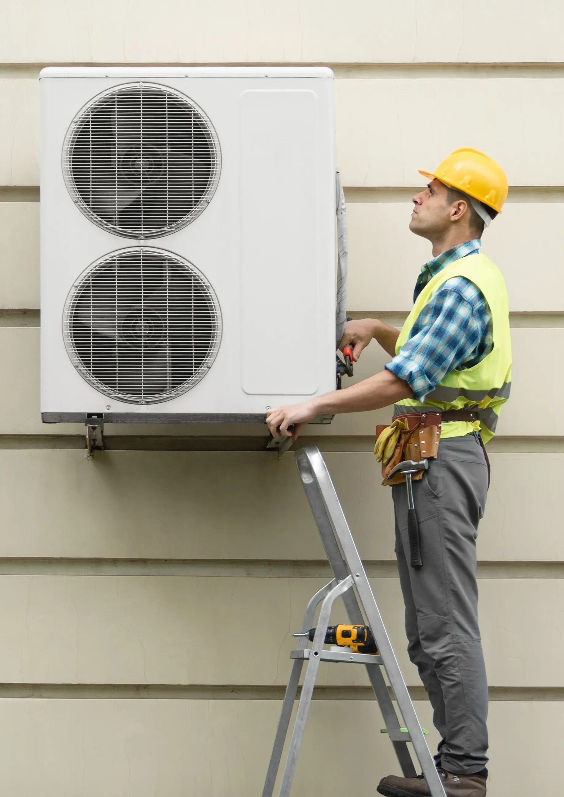 HVAC technician on ladder installing outdoor heat pump unit on building wall.