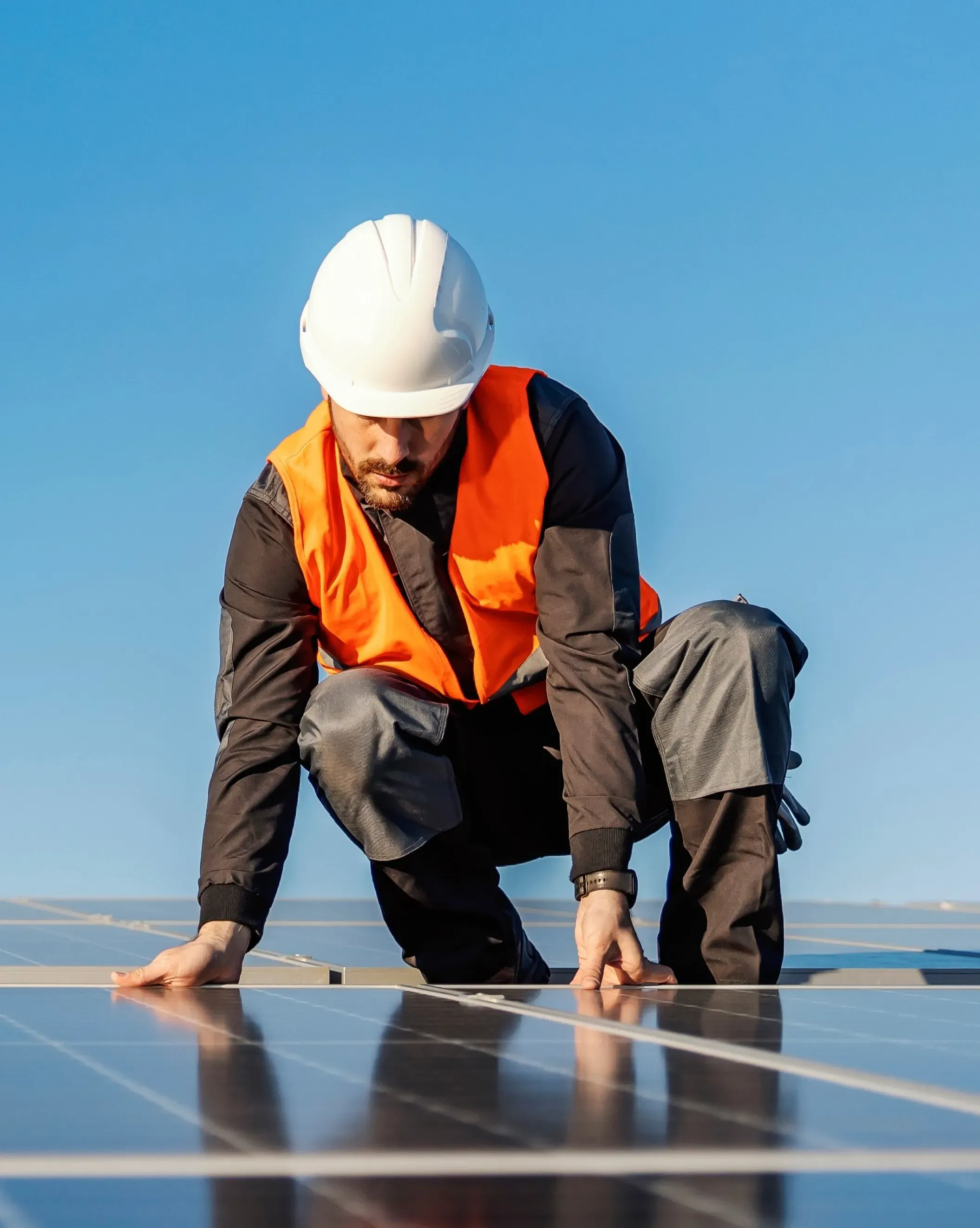 Trabajador de construcción en cuclillas sobre instalación de panel solar.