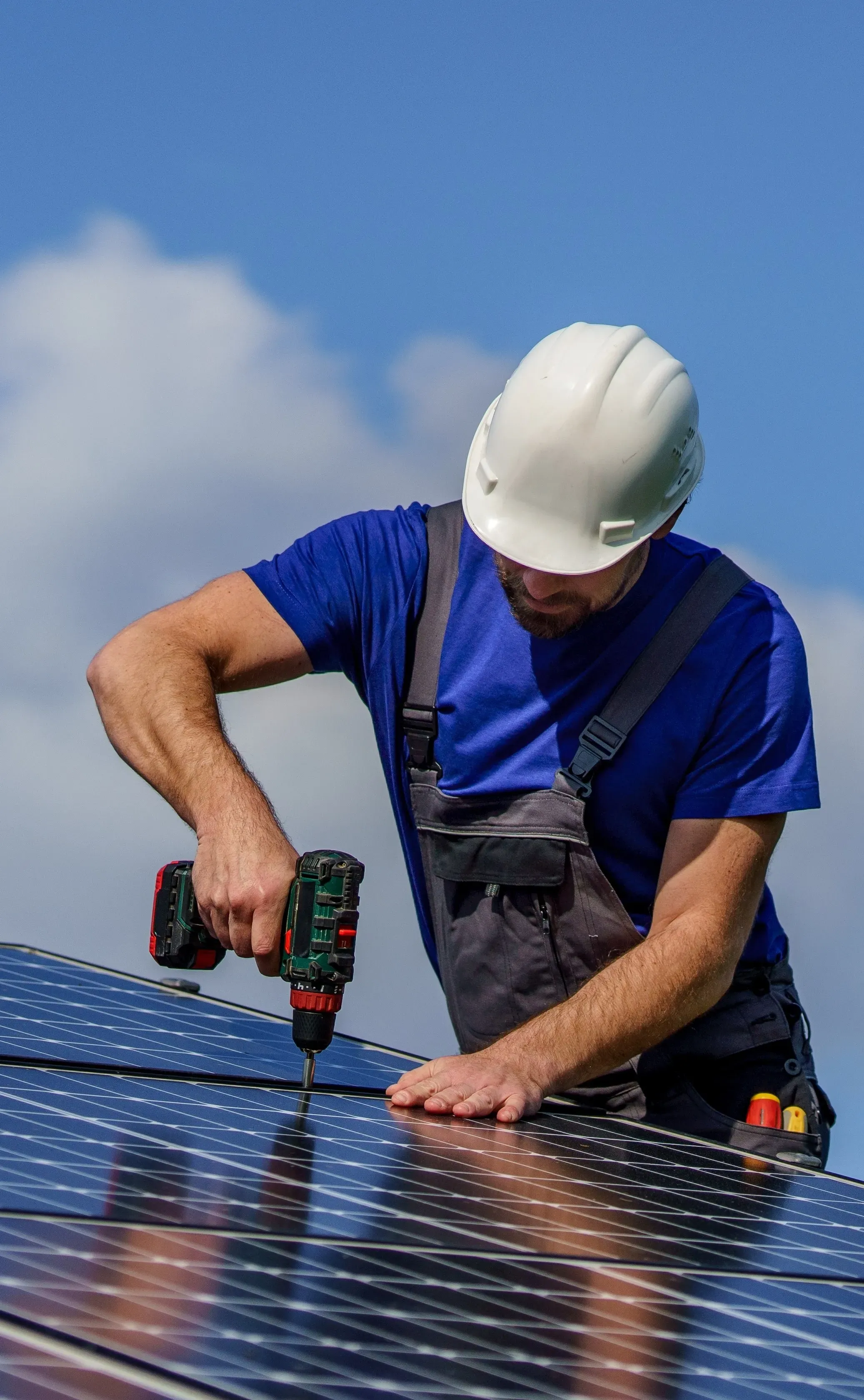 Trabajador instalando panel solar con taladro en tejado.