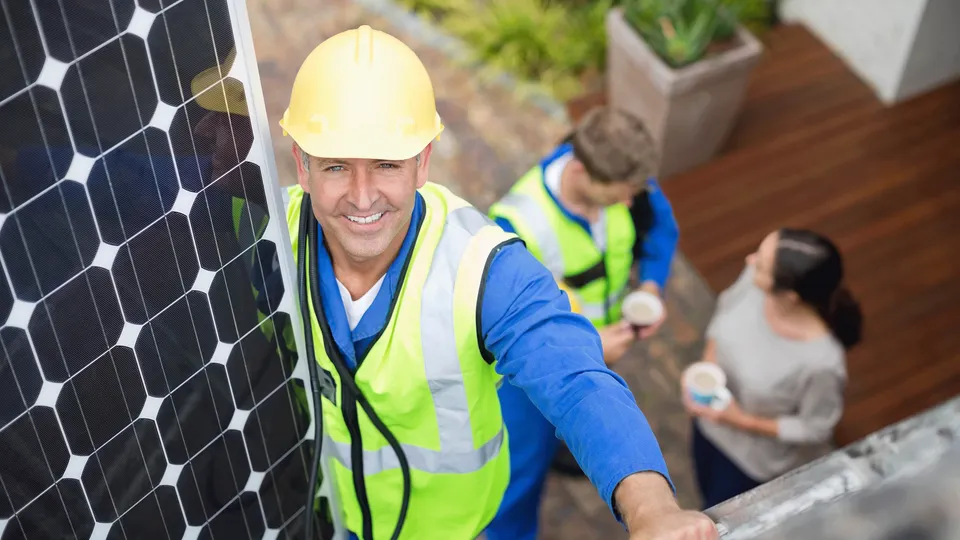 Solar panel installer smiling to camera on rooftop.