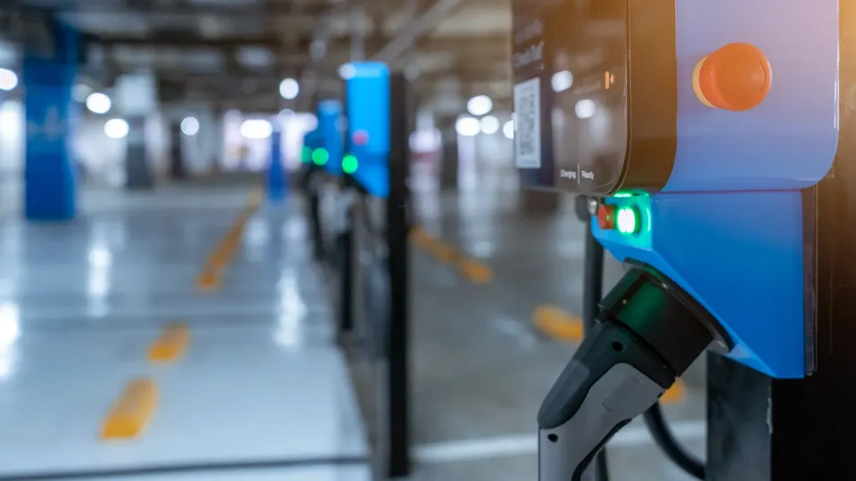 Elektrisk køretøjs ladekabel tilsluttet blå ladestation i parkeringshus.