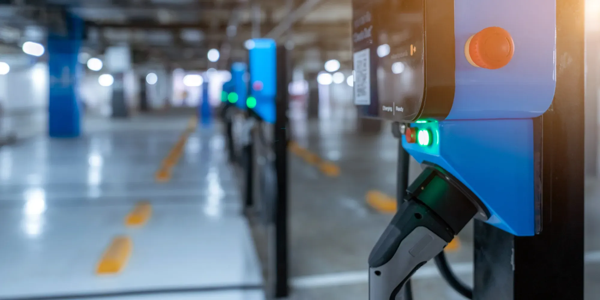 Elektrisk køretøjs ladekabel tilsluttet blå ladestation i parkeringshus.