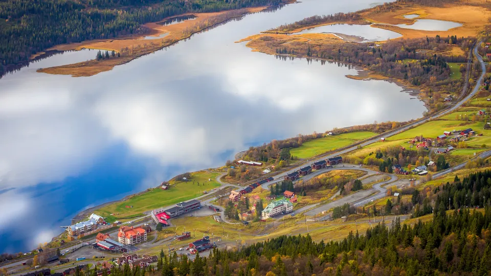 Flygfoto över Åre med älv, skogbevuxna berg och kustby.