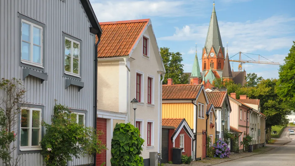 Färgglada historiska hus längs en kullerstensgata i Västervik med ett rött tegeltorn i bakgrunden.