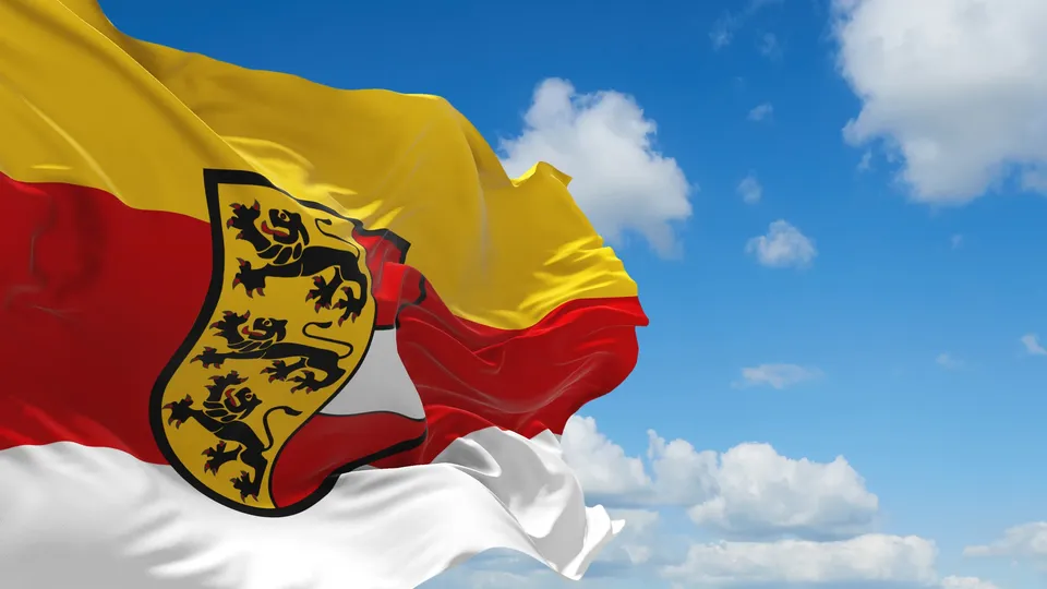 Gelb-rot-weiße Flagge Kärntens mit dem Kärntner Wappen vor blauem Himmel mit Wolken.