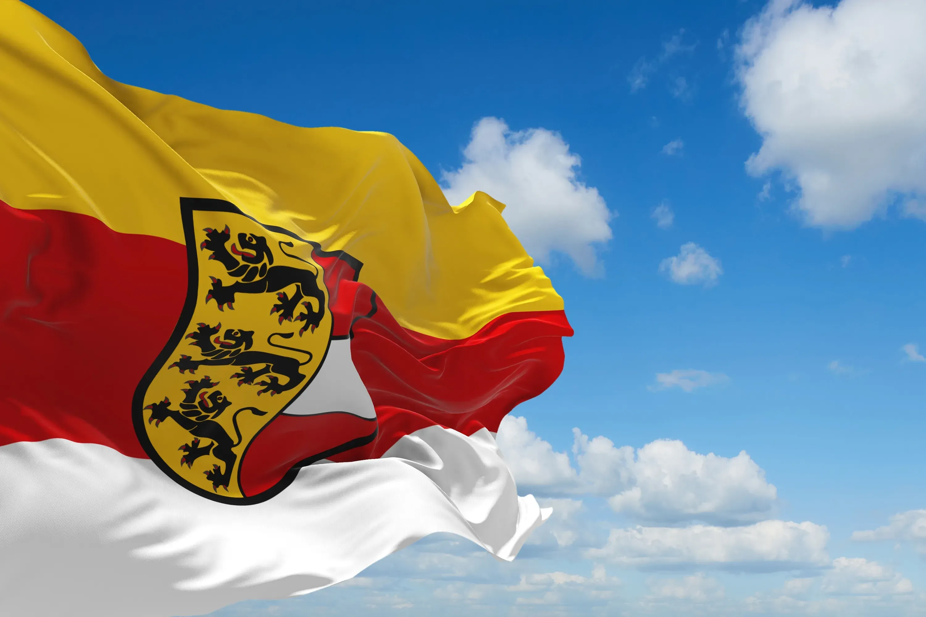 Gelb-rot-weiße Flagge Kärntens mit dem Kärntner Wappen vor blauem Himmel mit Wolken.