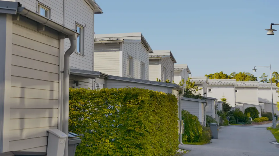 Rad av moderna kedjehus med gröna häckar längs en stenlagd gata.