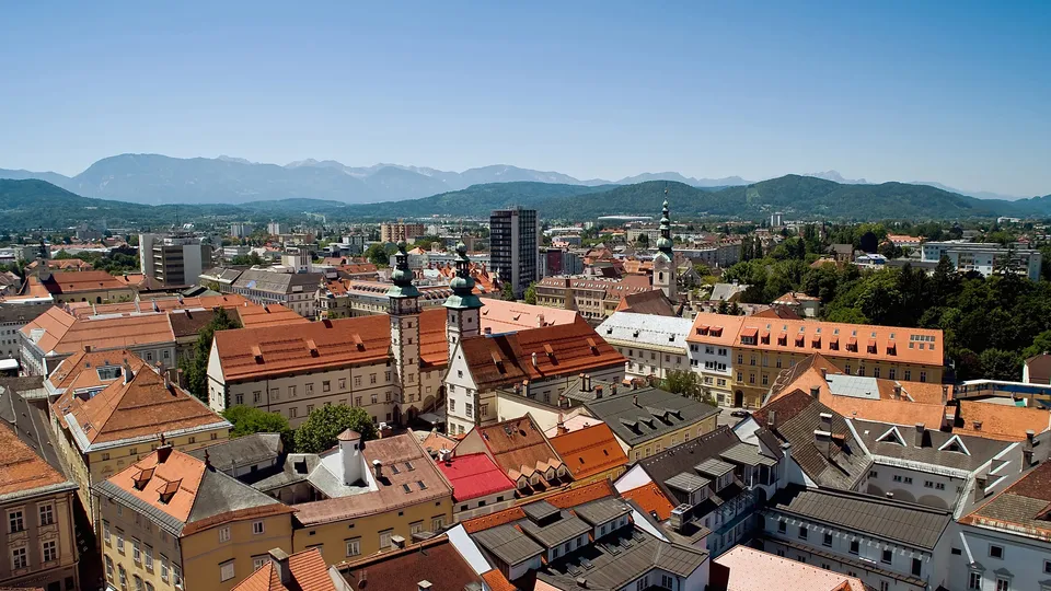 Blick über die Dächer von Klagenfurt mit historischen Gebäuden und den Bergen im Hintergrund.