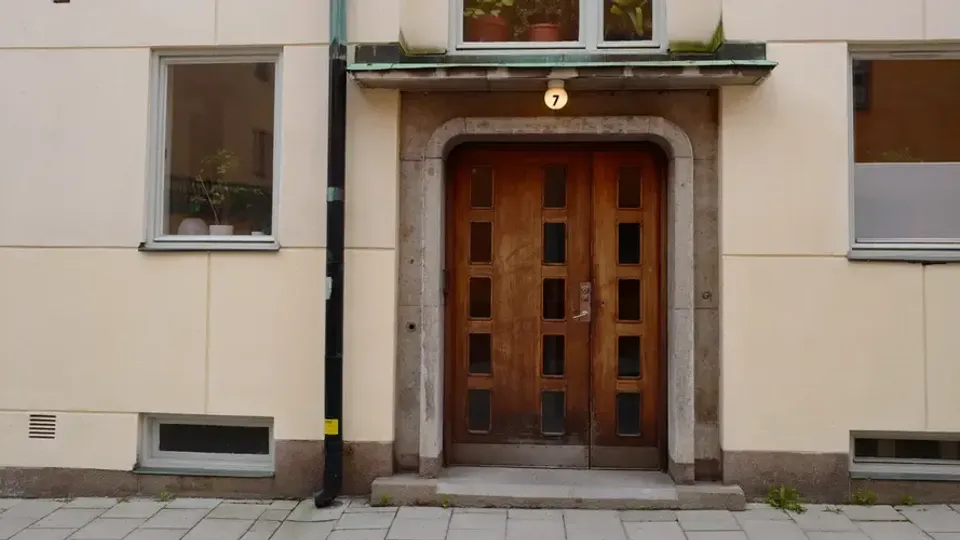 Entré till ett flerbostadshus med en brun port och ljus fasad, sedd från gatan.