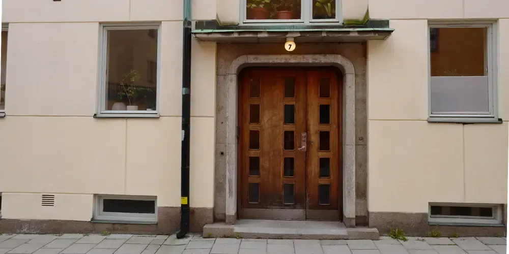 Entré till ett flerbostadshus med en brun port och ljus fasad, sedd från gatan.