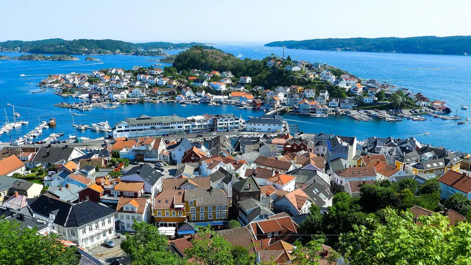 Luftfoto av kystby med fargefulle hus, marina og båter på blått vann.