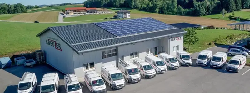 Elektromontagen Kreuzer GmbH & Co KG – Luftaufnahme des Firmengebäudes mit Photovoltaikanlage auf dem Dach und Fuhrpark aus Servicefahrzeugen