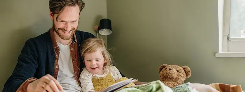 Bilde av en smilende far som leser i en bok for et lite barn