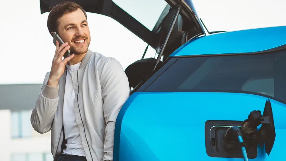 Mand taler i telefon ved siden af blå elektrisk bil med åben ladepport.