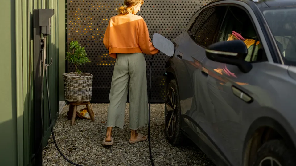 Kvinne lader elektrisk kjøretøy ved hjemmeladestasjonen.