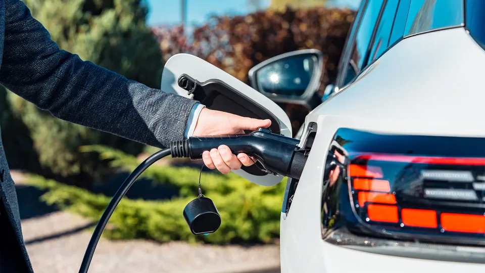 Person holder elbil-ladekabel tilsluttet hvid bil.
