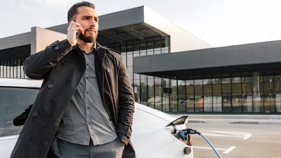 Mand på telefon står ved elbil-ladestation.