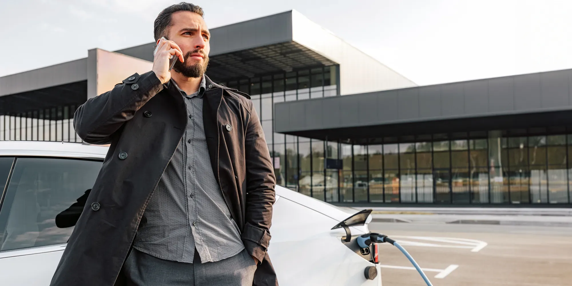 Mand på telefon står ved elbil-ladestation.