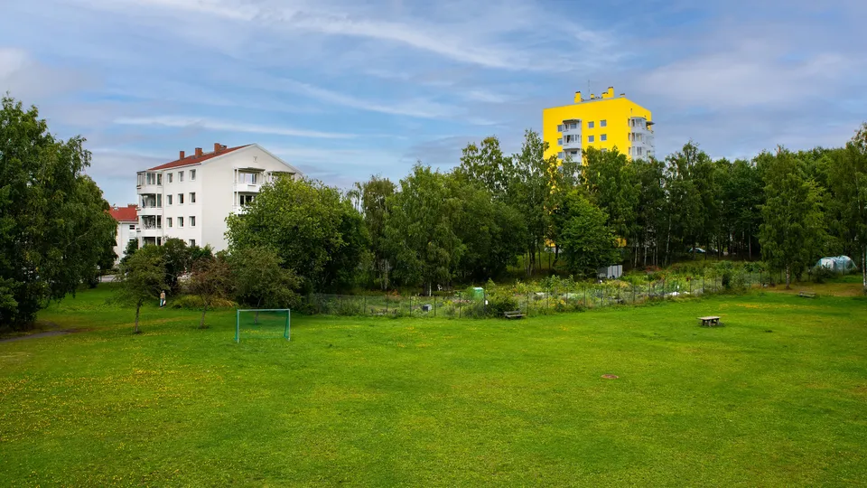 Grønn boligtomt med fotballmål, piknikbord og leilighetsbygg.