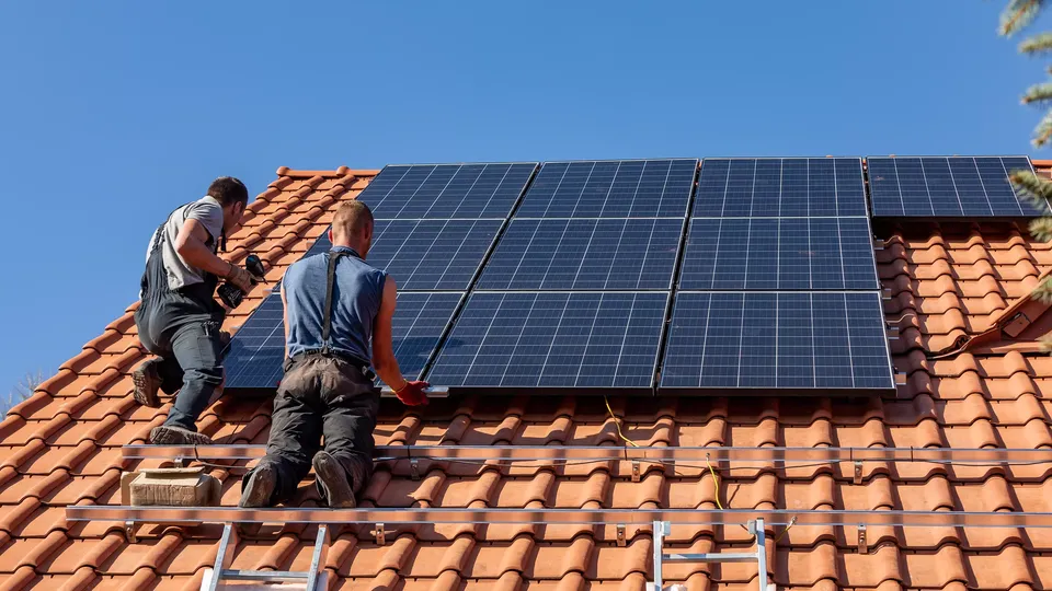 To danske solcellemontører er i gang med at installere solceller på et rødt tag