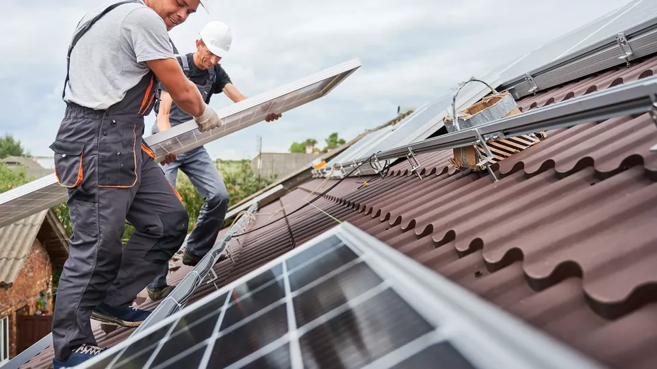 To solcellemontører løfter solceller, fordi de er ved at installere dem på taget