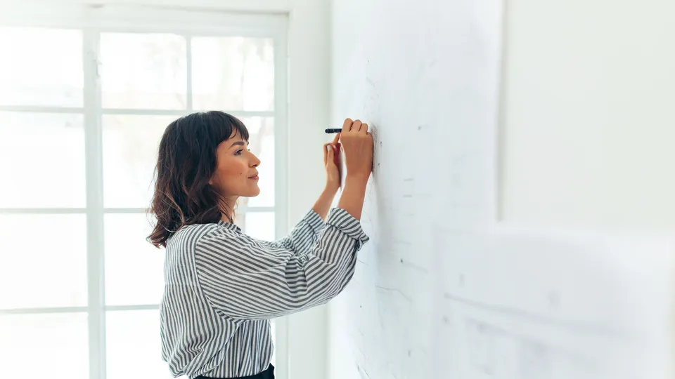 Kvinne skriver på whiteboard med en tusj.