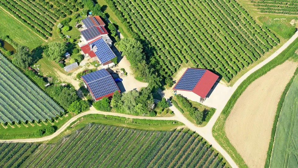 Luftaufnahme von Farmgebäuden mit Solaranlagen umgeben von Agrarflächen.