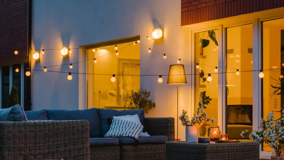 Udendørs terrasse med havemøbler og lyskæder i skumringen.