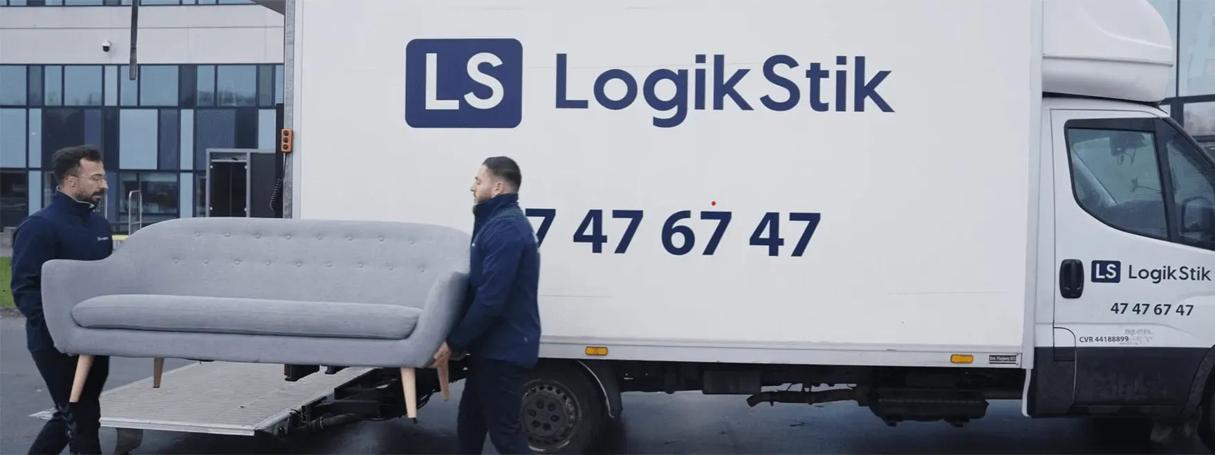 LogikStik flyttemænd bærer på en sofa foran en af firmaets flyttevogne.