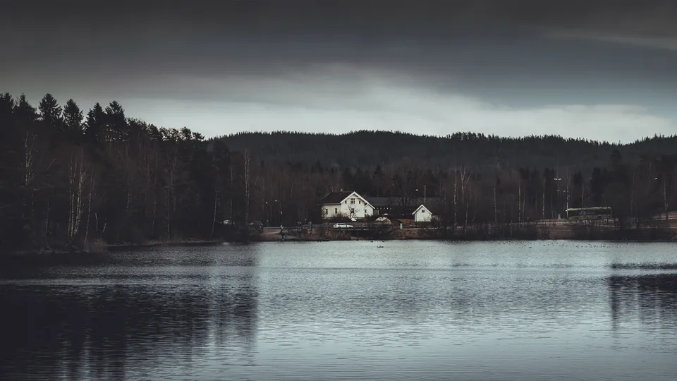 Hvite hus på en skogkledt strandlinje over stille vann.