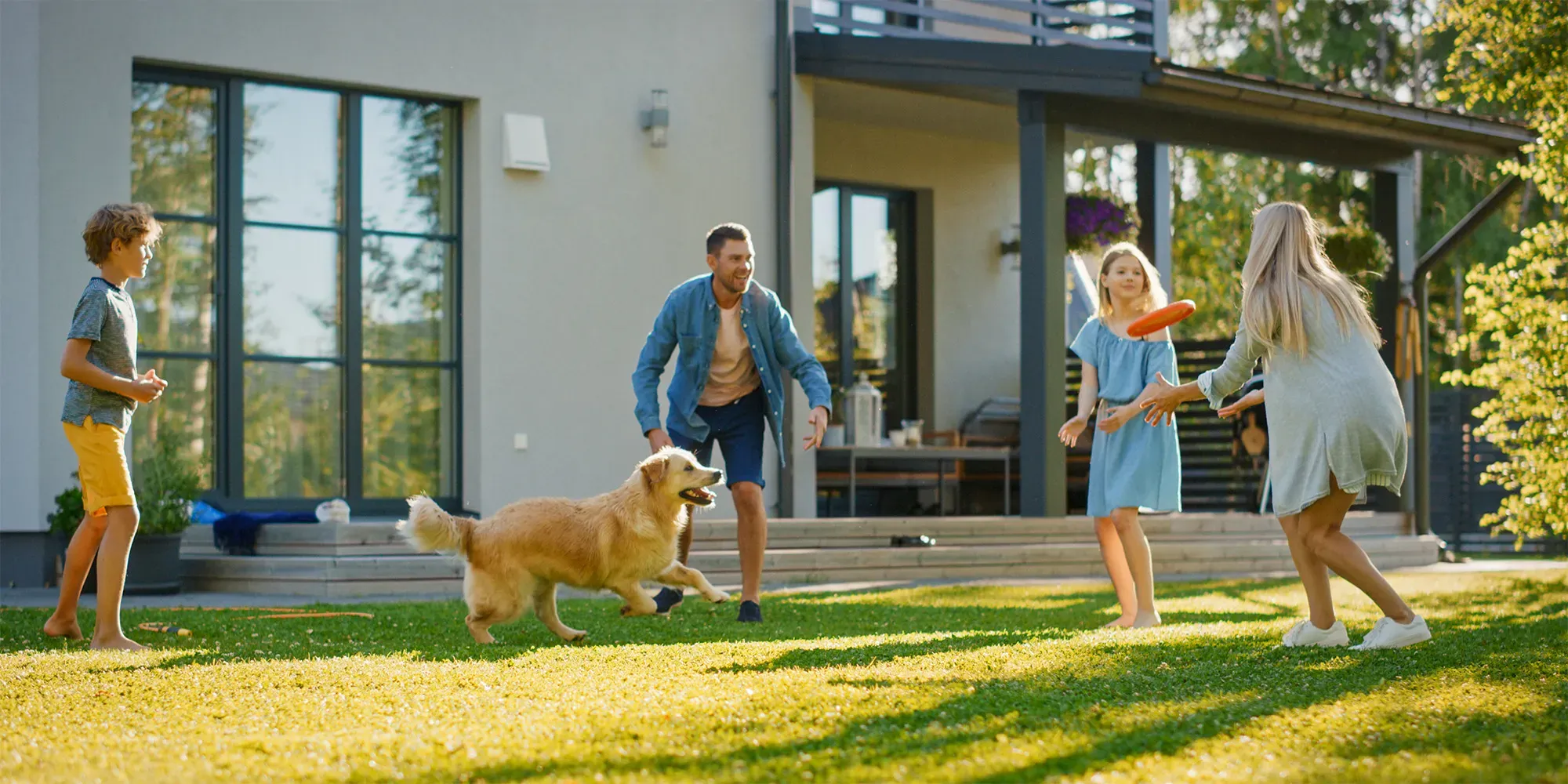 Familie spiller frisbee med hund i baghaven.