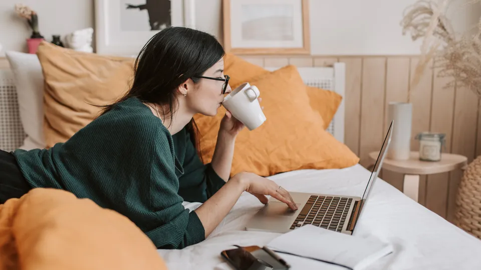 Kvinne drikker kaffe mens hun jobber på PC.