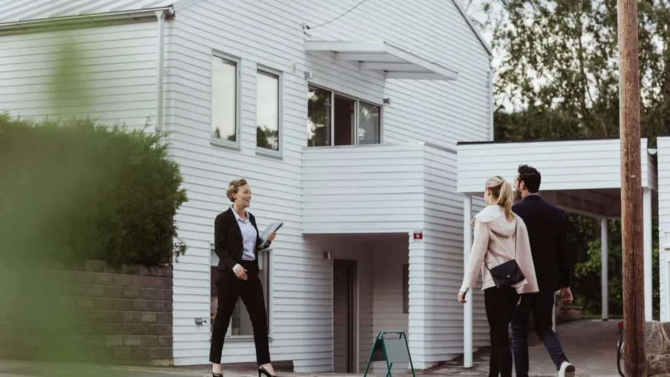 Fastighetsmäklare visar en vit trävilla för ett par.