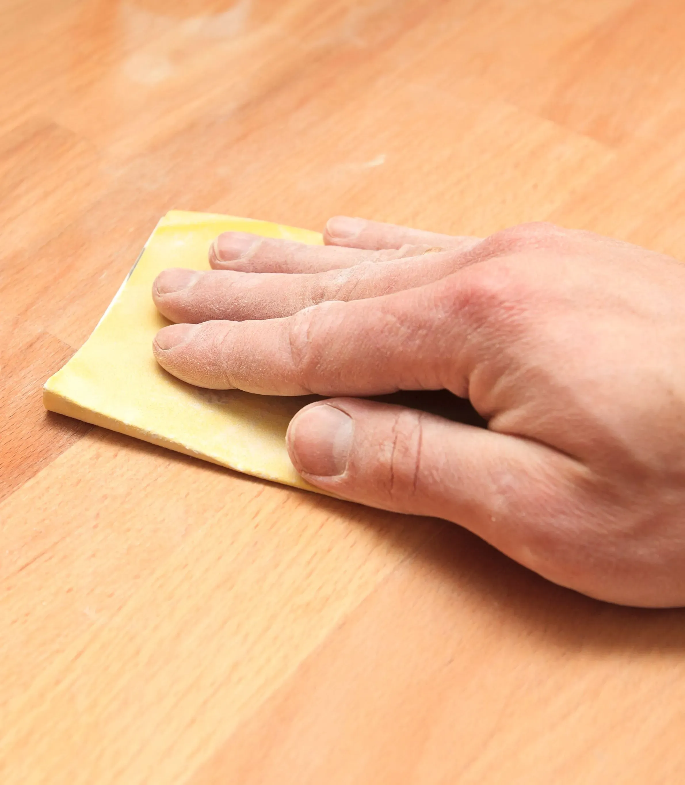 Hand pusser treflate med gult sandpapir.