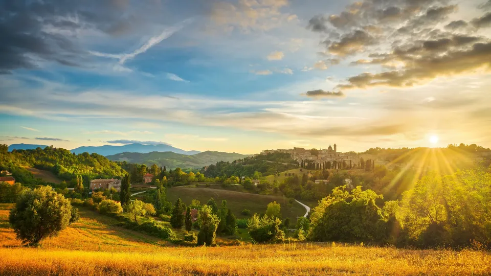 Paesaggio della campagna toscana al tramonto con colline ondulate, cipressi e villaggio in lontananza.