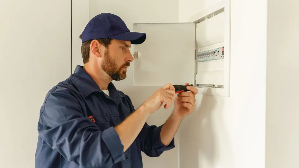 Elektriker inspiserer elektrisk panel med skrutrekker.