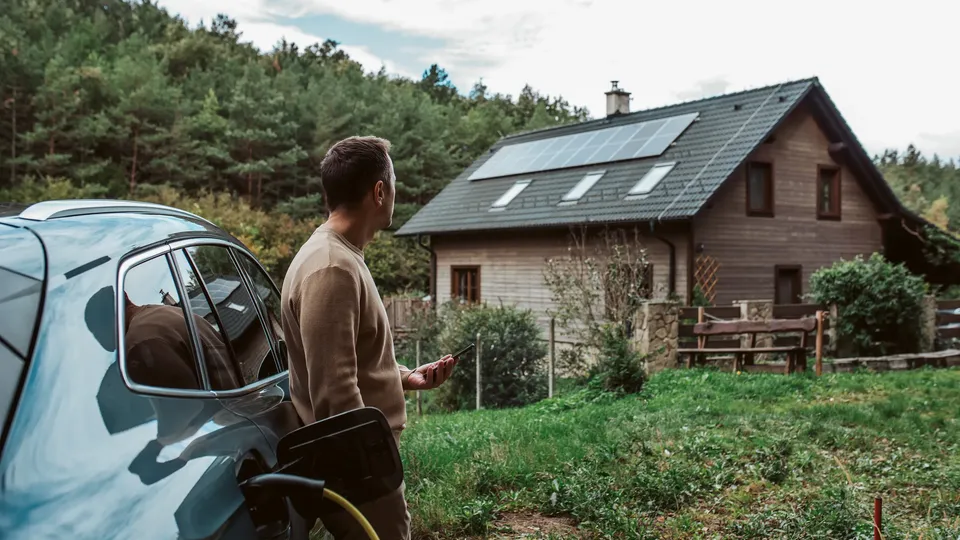 Mann som står ved elbil ved hus med solcellepaneler.