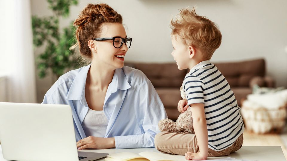 Bilde av en kvinne som smiler mot barnet sitt som sitter på bordet ved siden av en laptop.