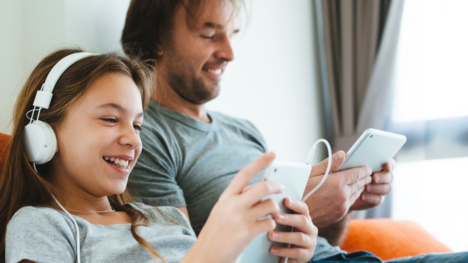 Bilde av en far og datter som sitter på hver sin mobiltelefonon og smiler ved siden av hverandre.