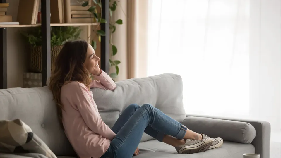 Kvinne sitter på sofa og ser mot vinduet.