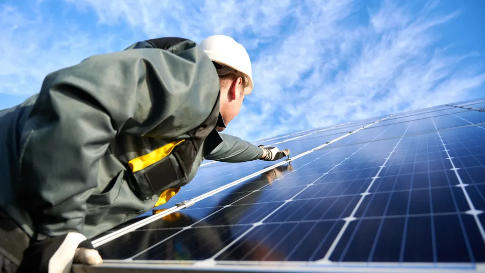 Trabajador instalando panel solar con herramienta amarilla en techo.