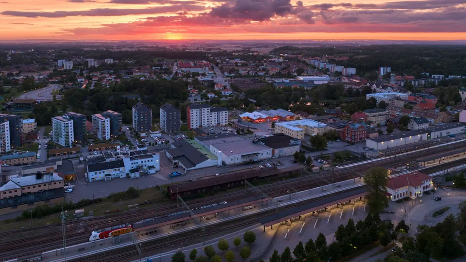 Utsikt över kvarter med lägenhetshus, träd, och en tågstation, under en rosa himmel.