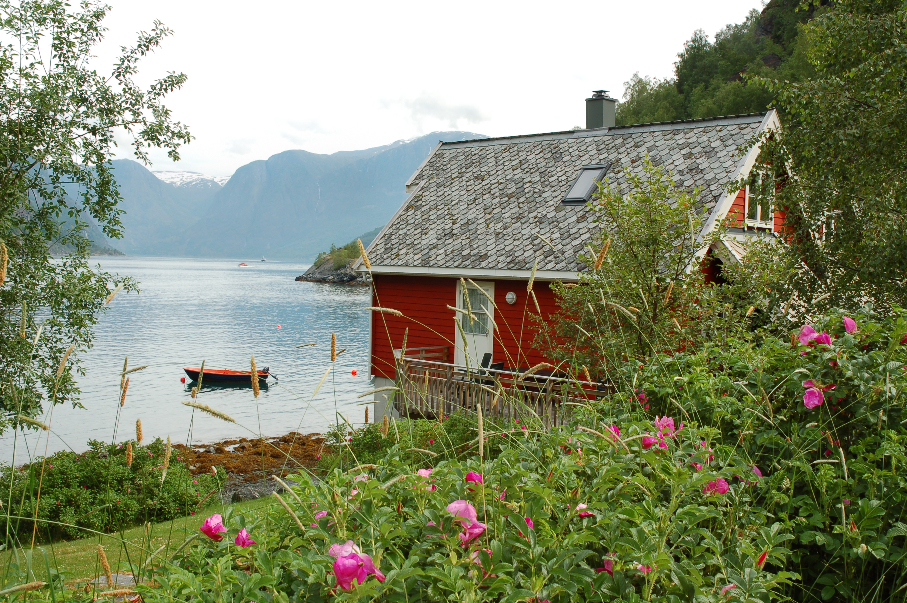 Fotografi av en rød hytte med en robåt på en fjord i bakgrunn